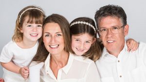 family of 4 at a studio photoshoot smiling and wearing white