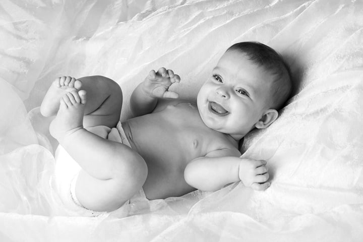 smiling, chuckling baby laying on back on white chiffon