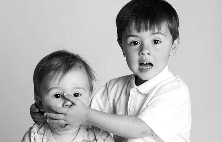humorous shot of two young brothers with hand over mouth