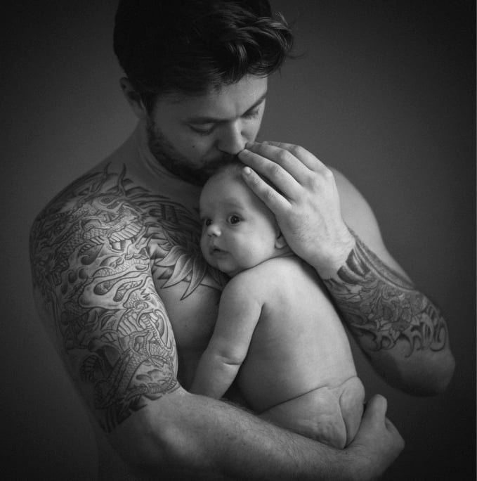 shirtless dad holding young baby against his body looking down kissing top of head