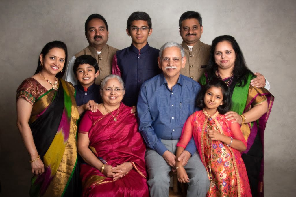 three generation portrait of an indian family of nine wearing brightly coloured saris