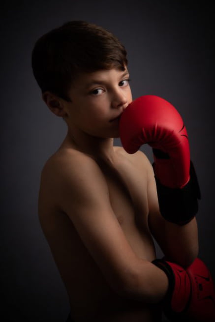 shy looking young lad with boxing gloves looking at camera out of corner of his eyes