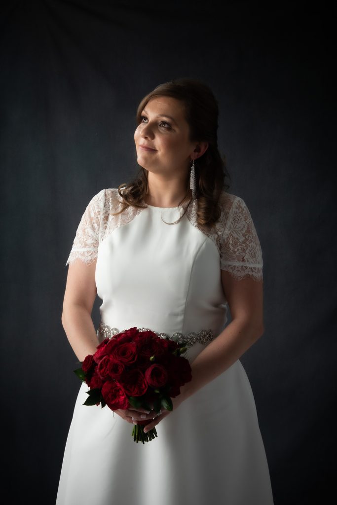 classic portrait of bride against dark background with red roses bocquet